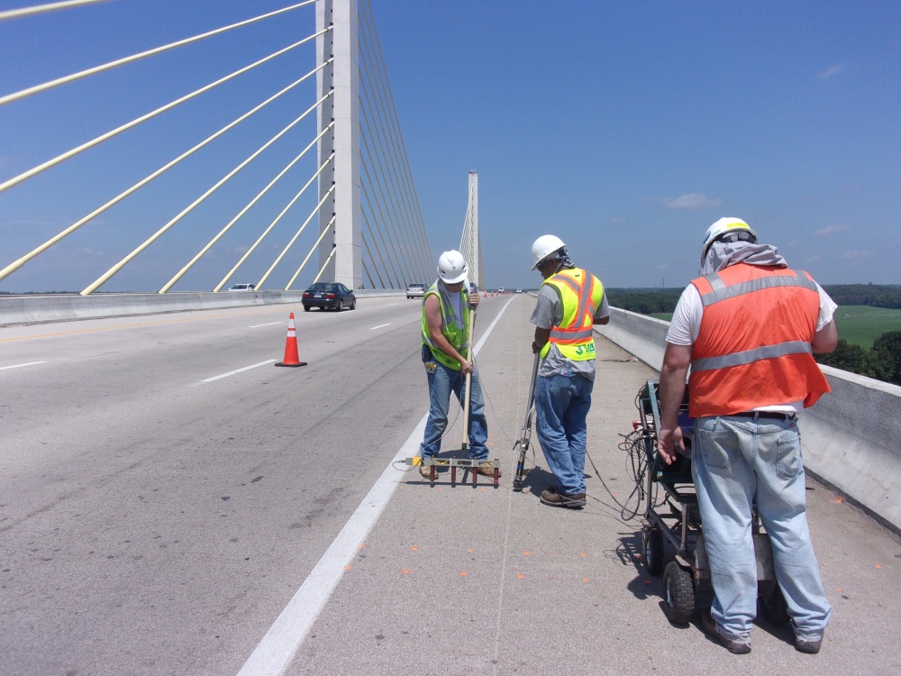 On a clear, sunny day, three engineers in PPE are standing on a bridge deck using GPR and IE/PV equipment.