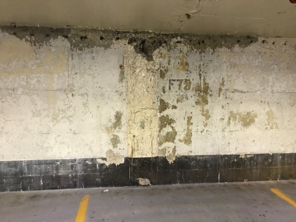 Wall with clear signs of corrosion at the ceiling. PT cables are corroding, spalling and cracked concrete visible and peeling paint.